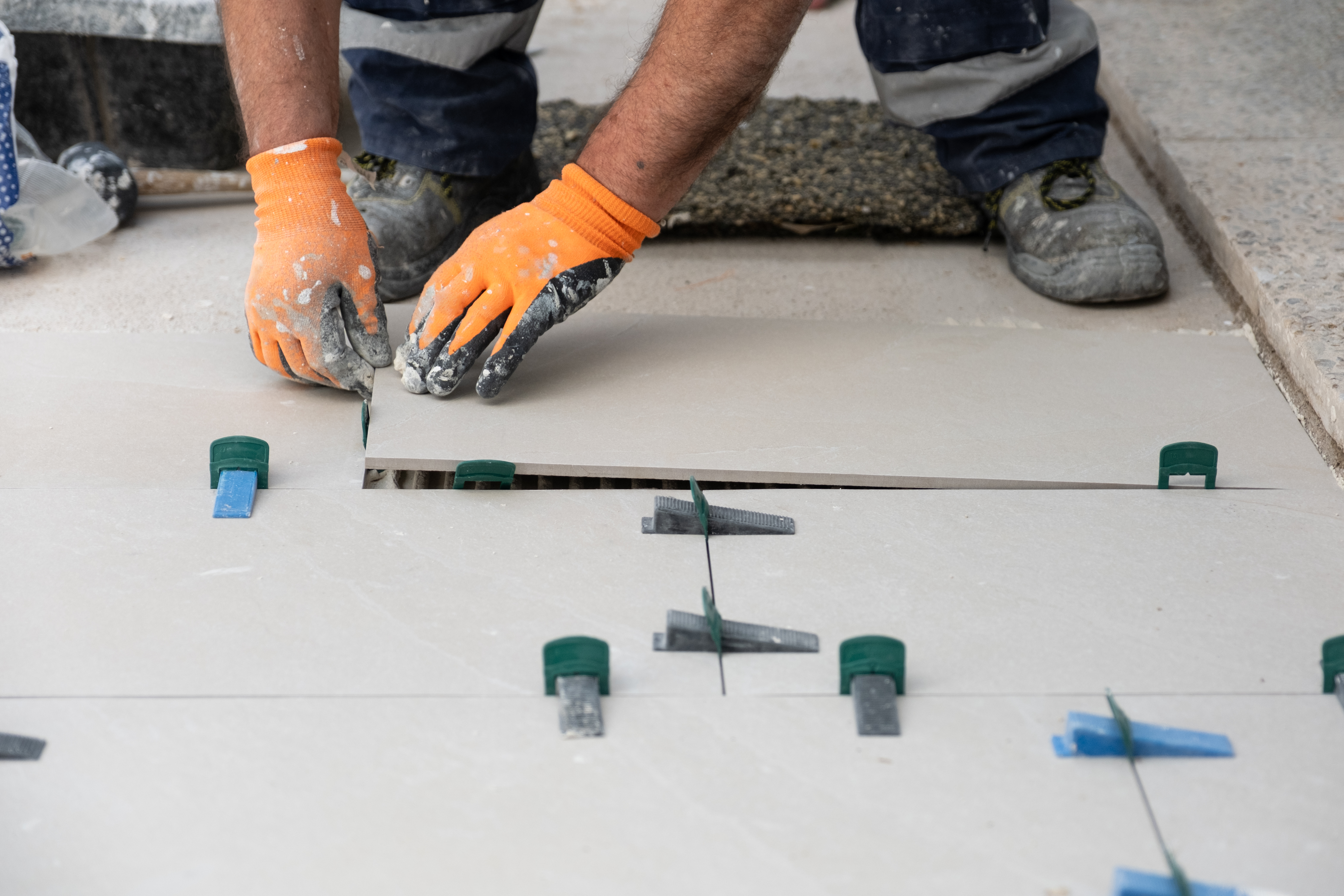 Worker hands laying down new floor tiles with spacers and wedges